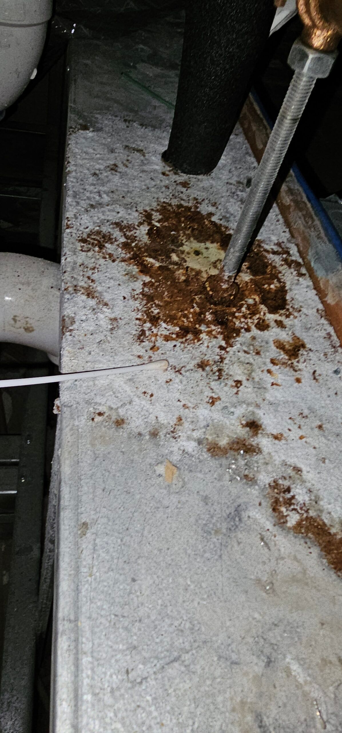 Rusty, stained surface with a pipe and tool, possibly in a basement.