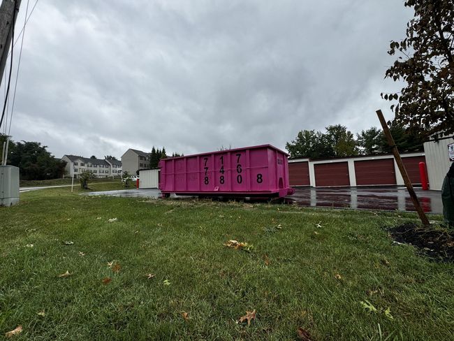 A pink dumpster is sitting in the middle of a grassy field.