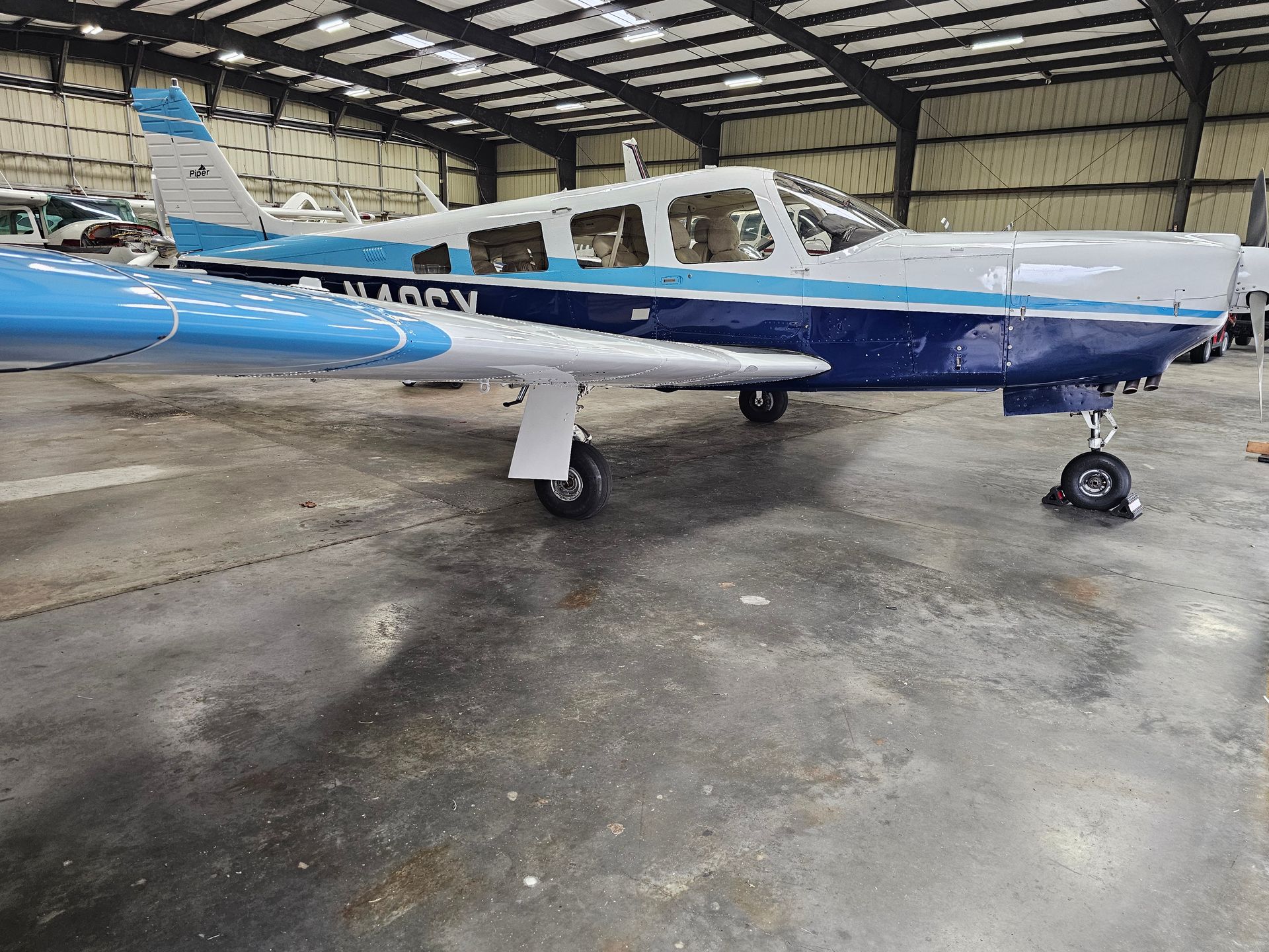 Blue and white single-engine airplane parked inside a hangar.