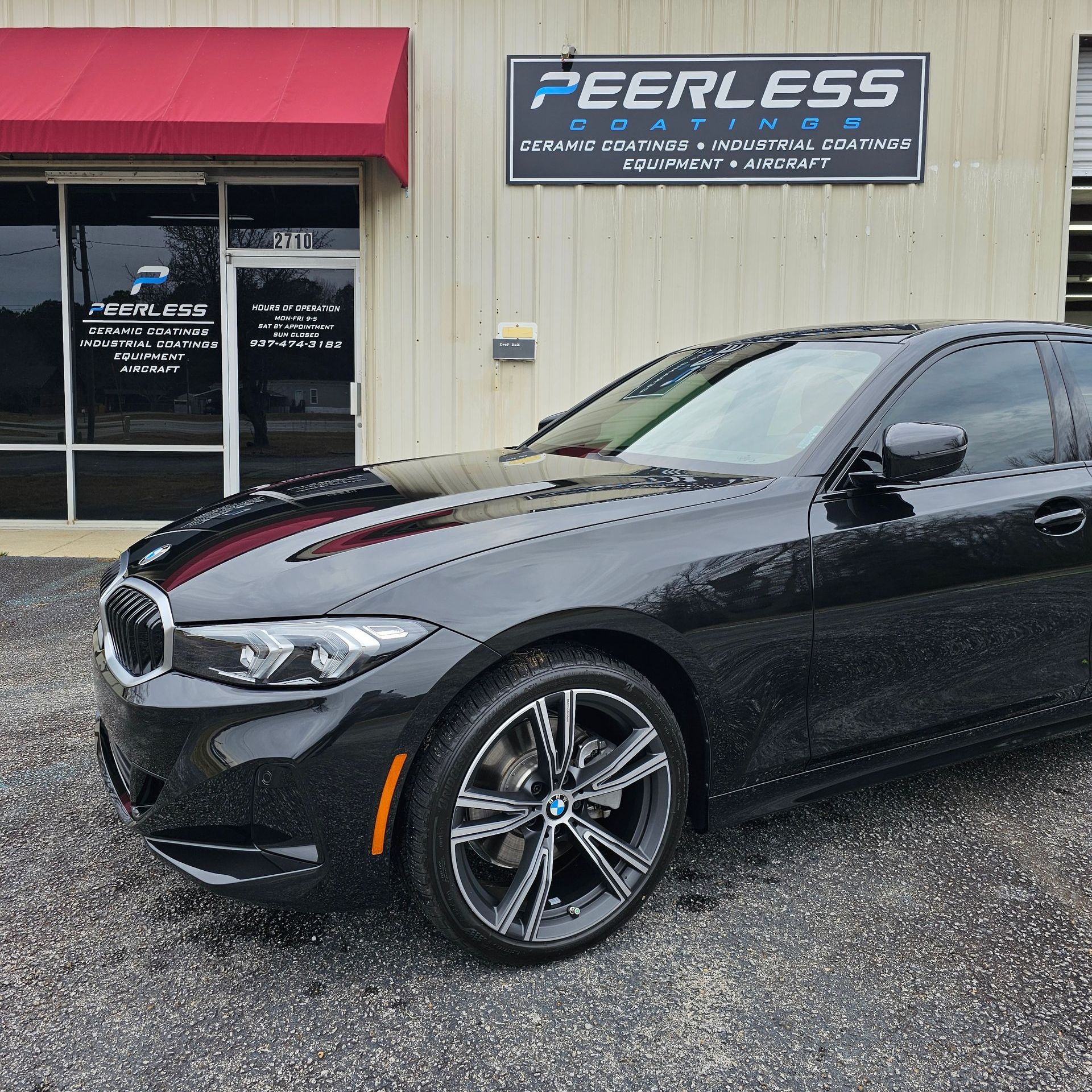 A black car is parked in front of a peerless coatings building