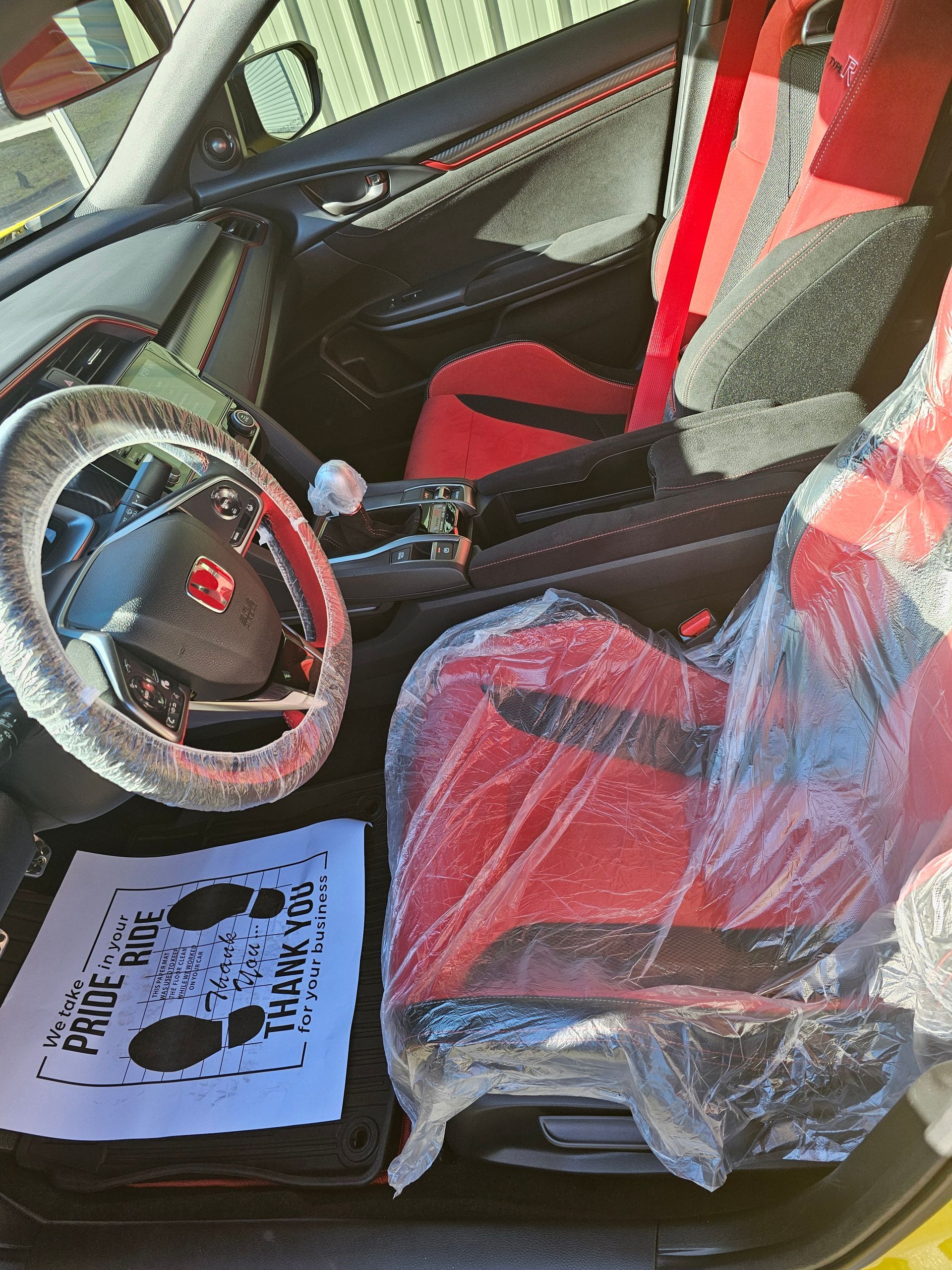 The inside of a car with a steering wheel and seats wrapped in plastic.
