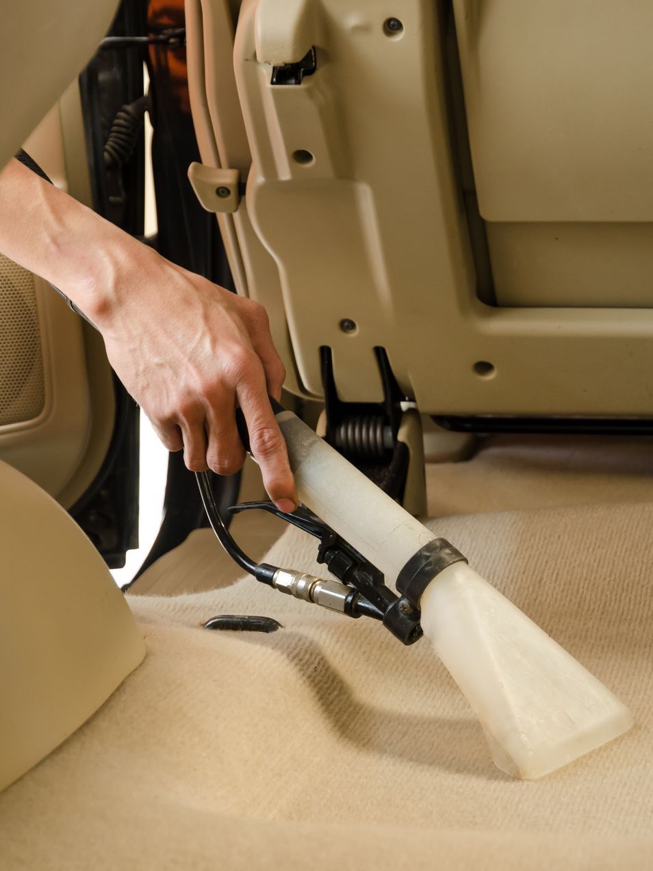 A person is using a vacuum cleaner to clean the carpet in a car.