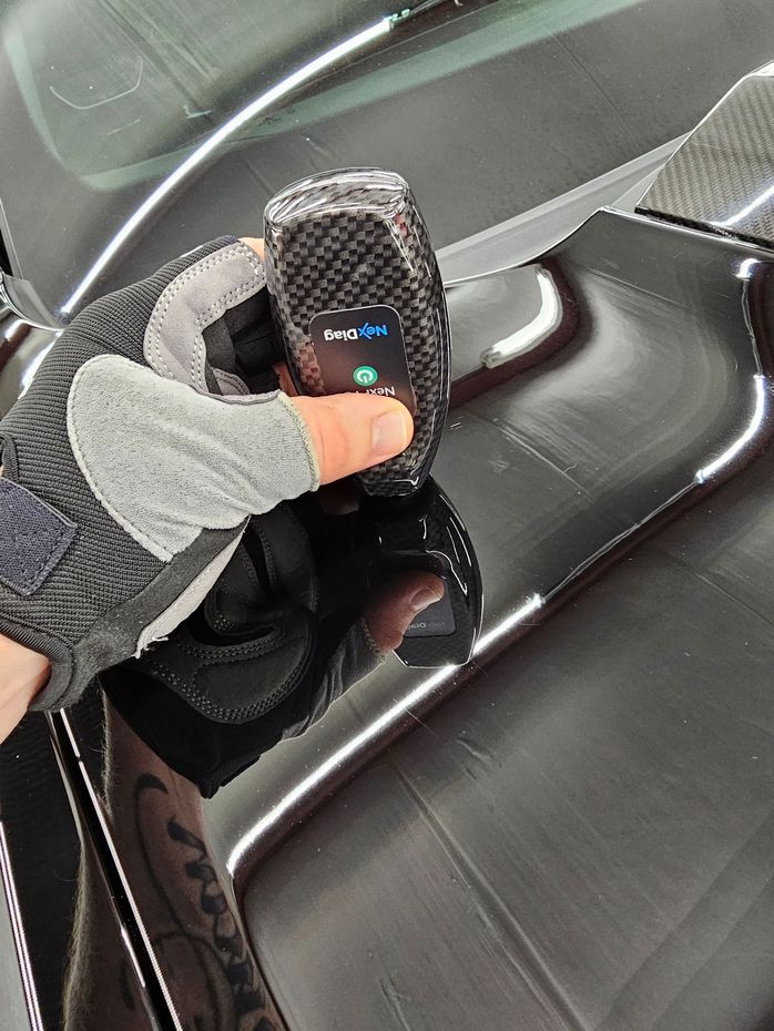 A person is holding a remote control in front of a car.