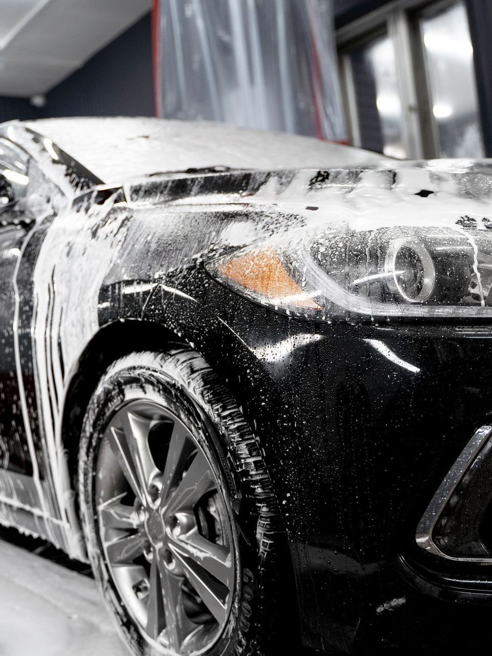 A black car is covered in foam in a garage.