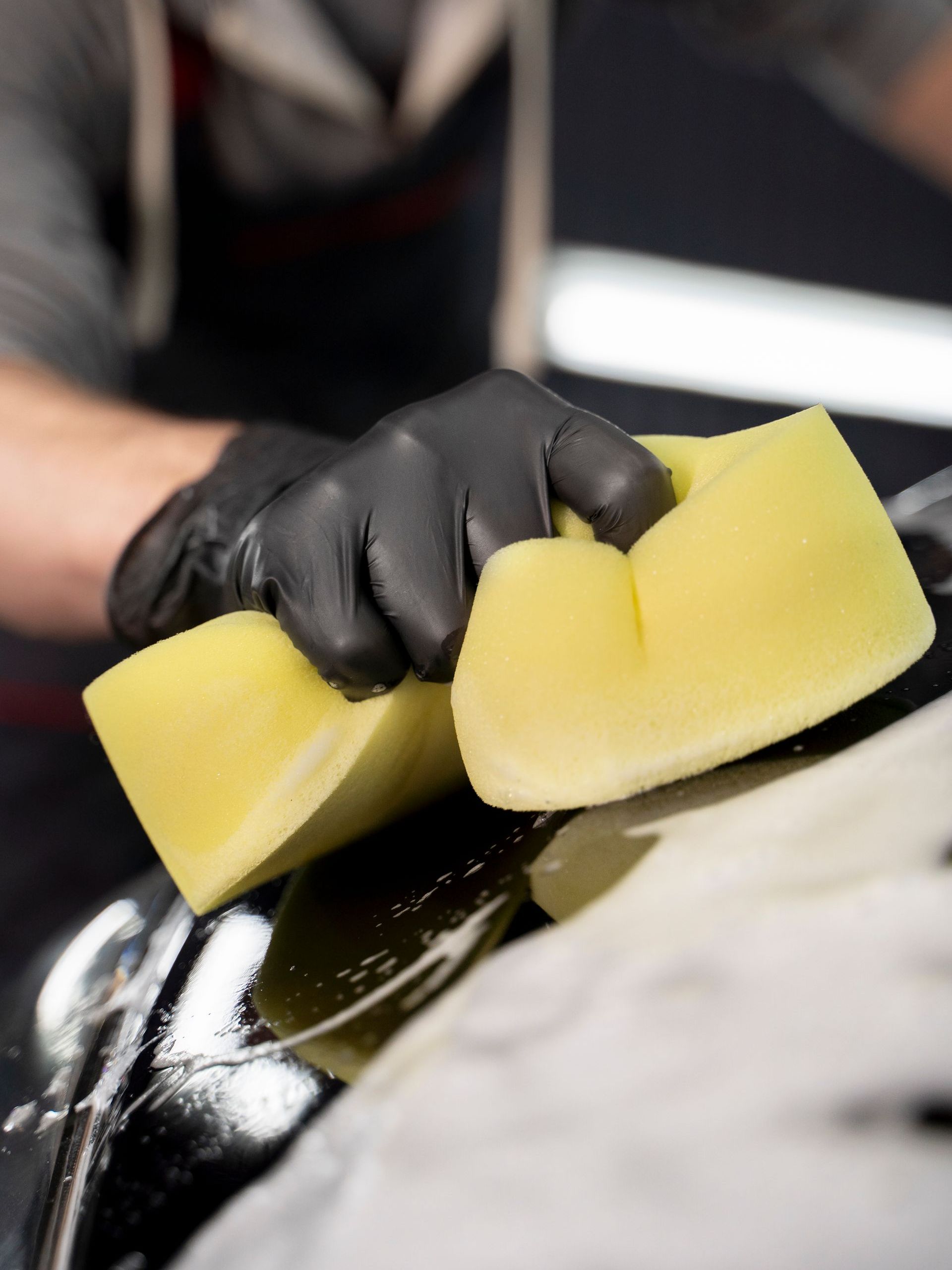 A man is cleaning a car with a yellow sponge.