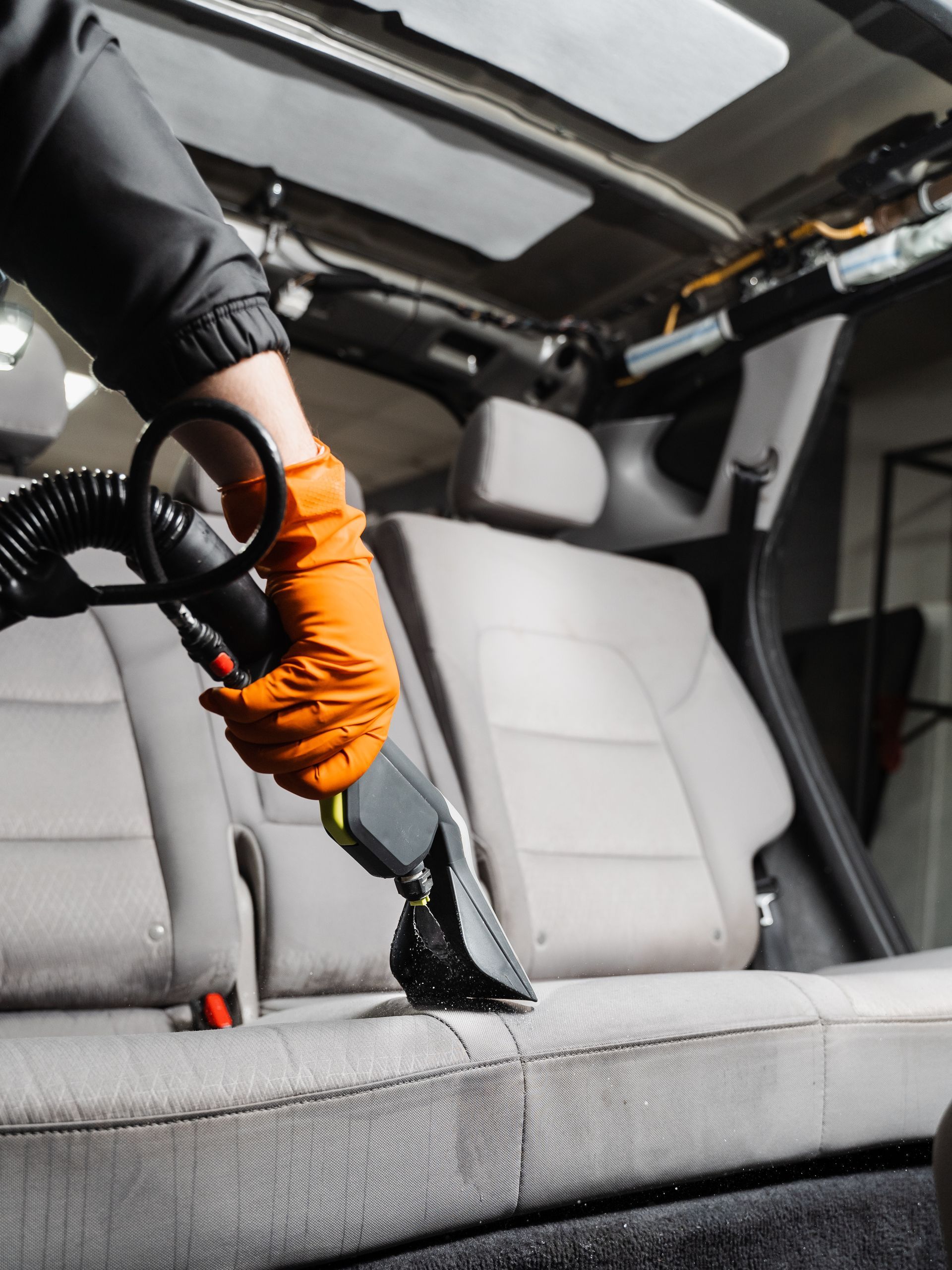 A person is cleaning the seats of a car with a vacuum cleaner.