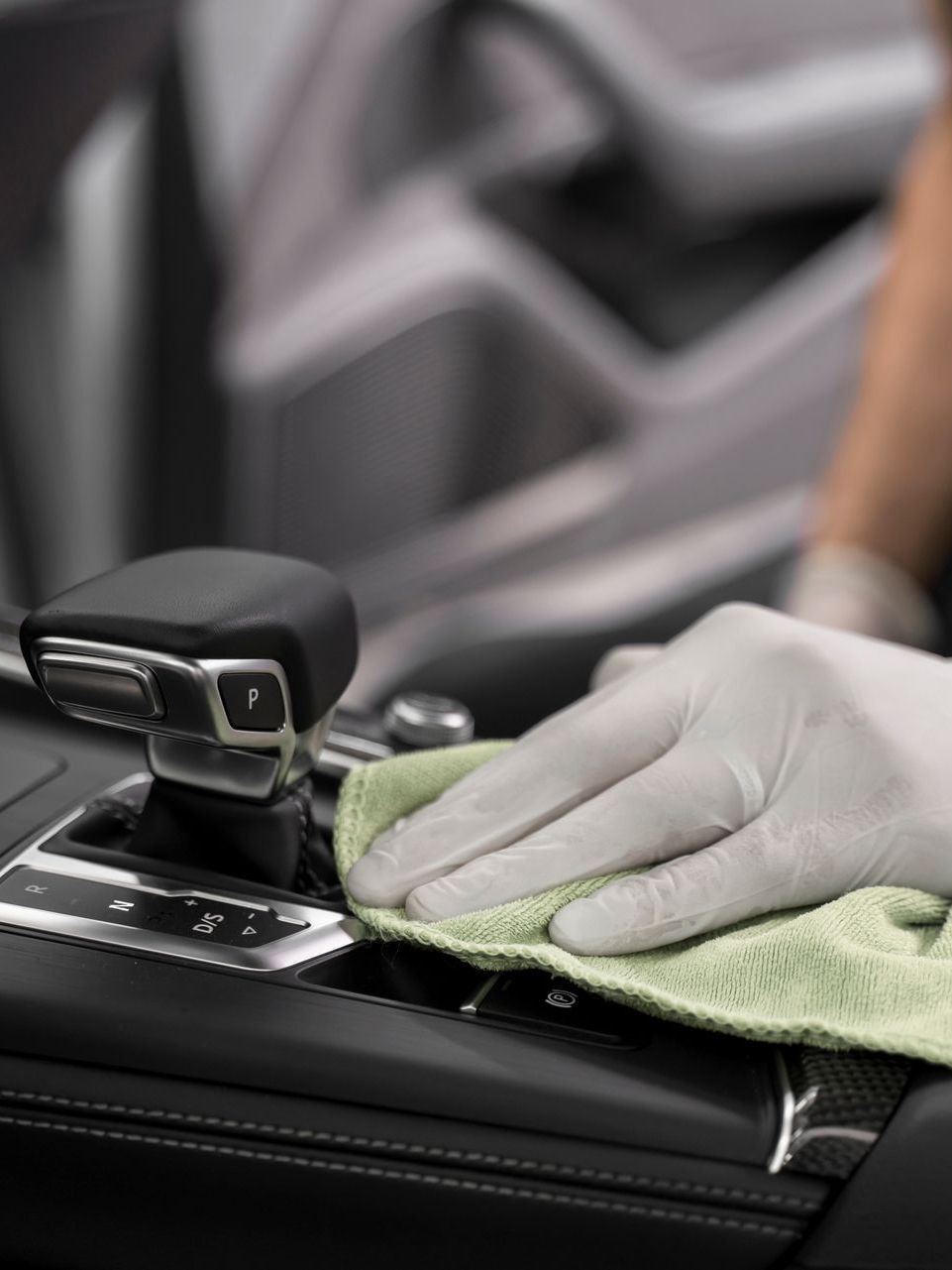 A person wearing gloves is cleaning the dashboard of a car with a cloth.