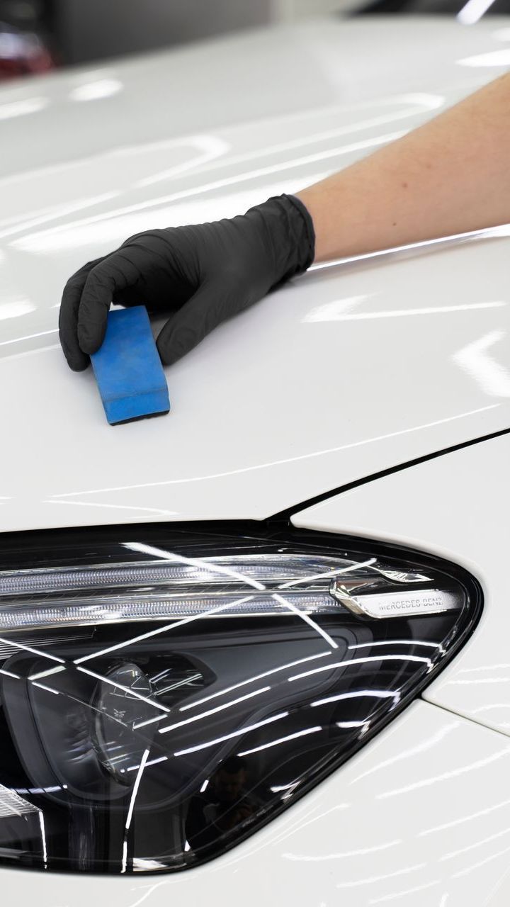 A person is cleaning the hood of a white car with a blue sponge.