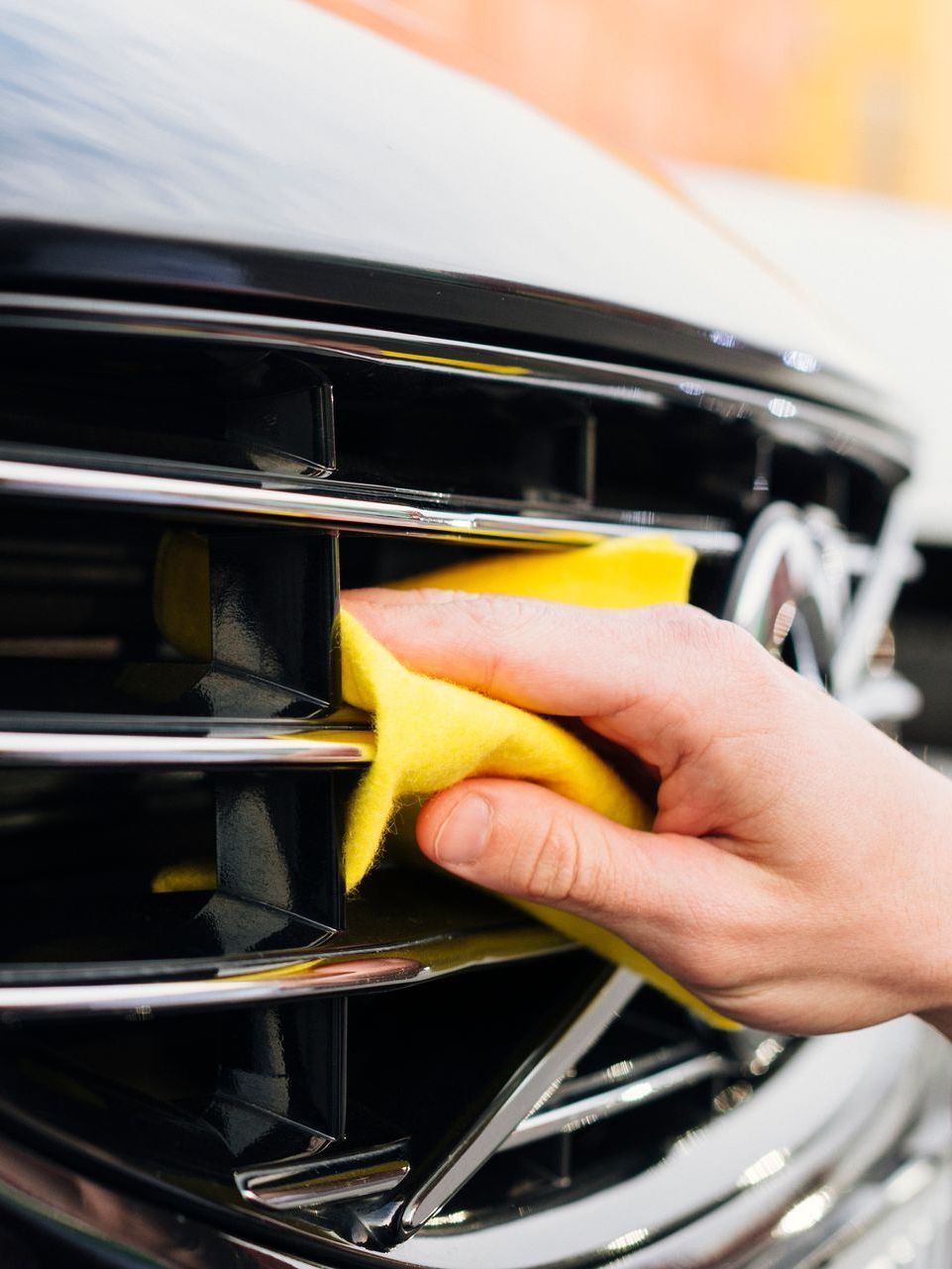 A person is cleaning the grille of a car with a yellow cloth.