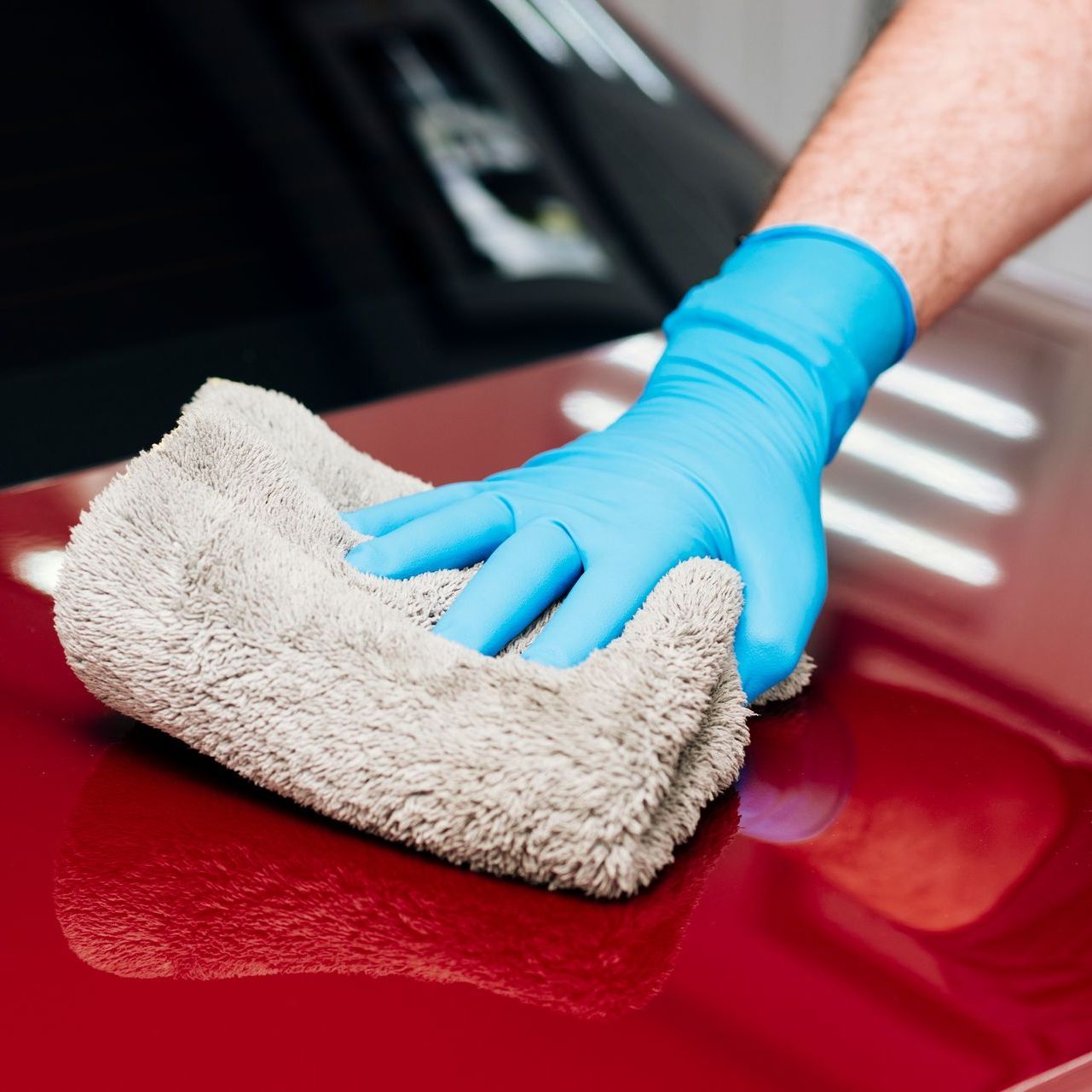 A person wearing blue gloves is cleaning a red car with a towel