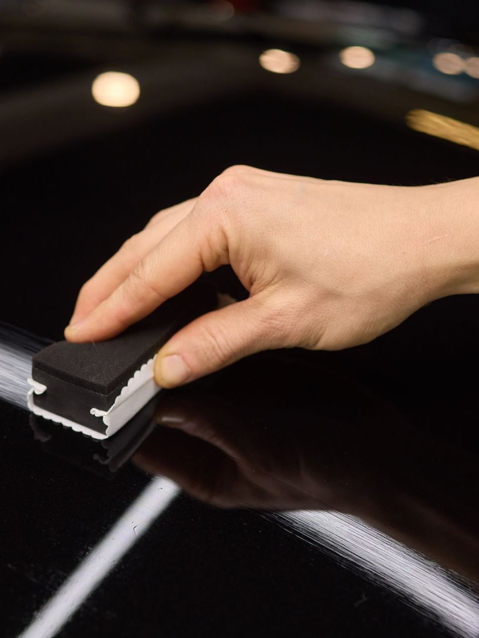 A person is polishing a black car with a sponge