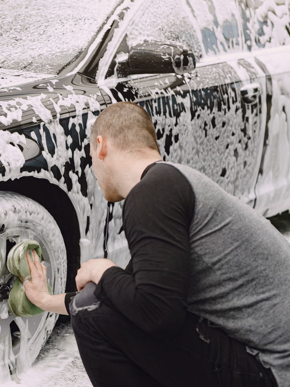 A man is kneeling down to wash a car with foam on it