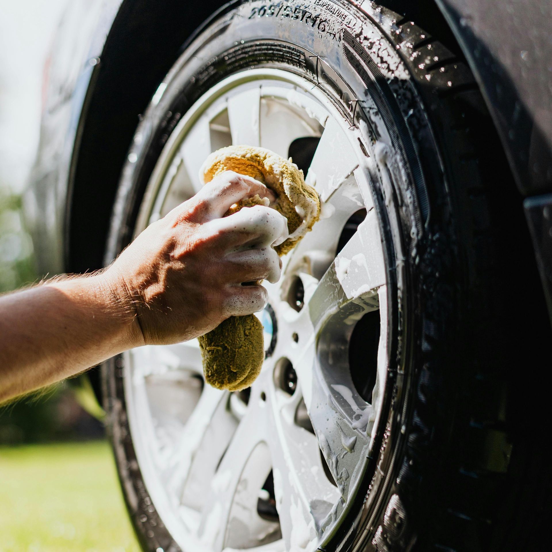 A person is washing a car wheel with a sponge.