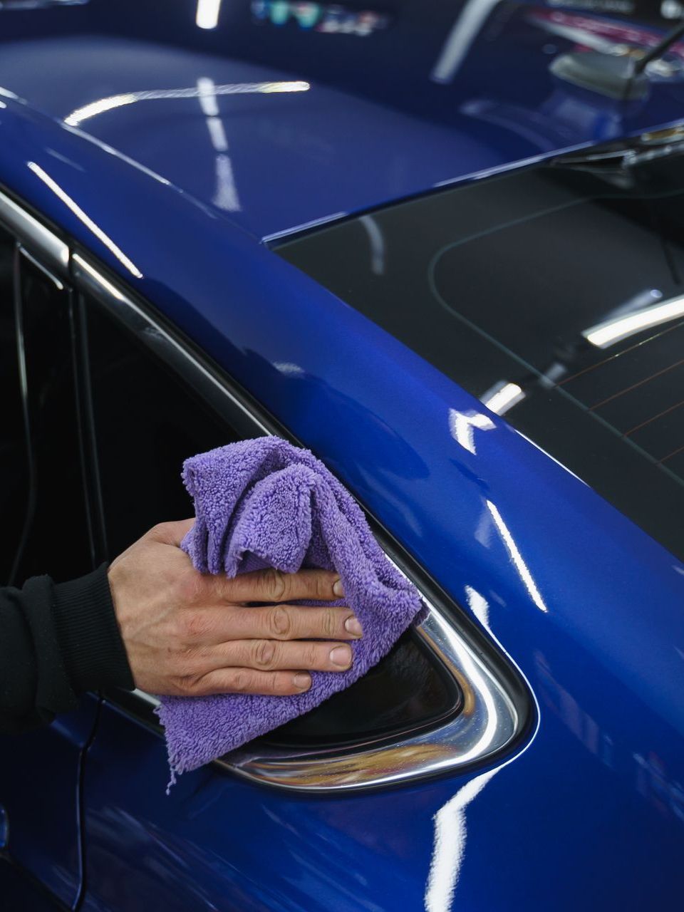 A person is cleaning a blue car with a purple towel.