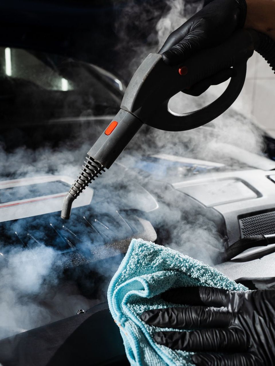 A person is cleaning a car with a steam cleaner.