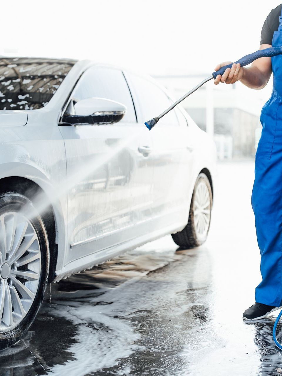 A man is washing a white car with a high pressure washer.