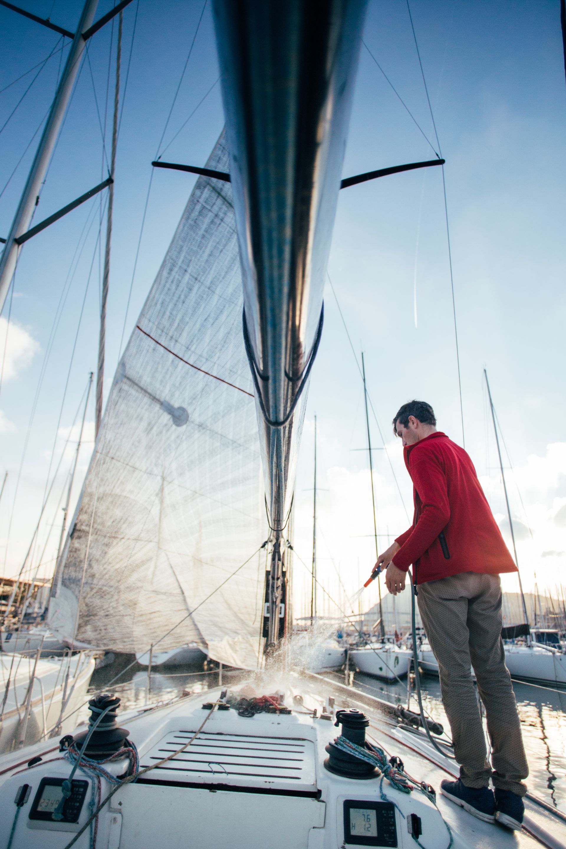 A man in a red jacket is standing on the deck of a sailboat.