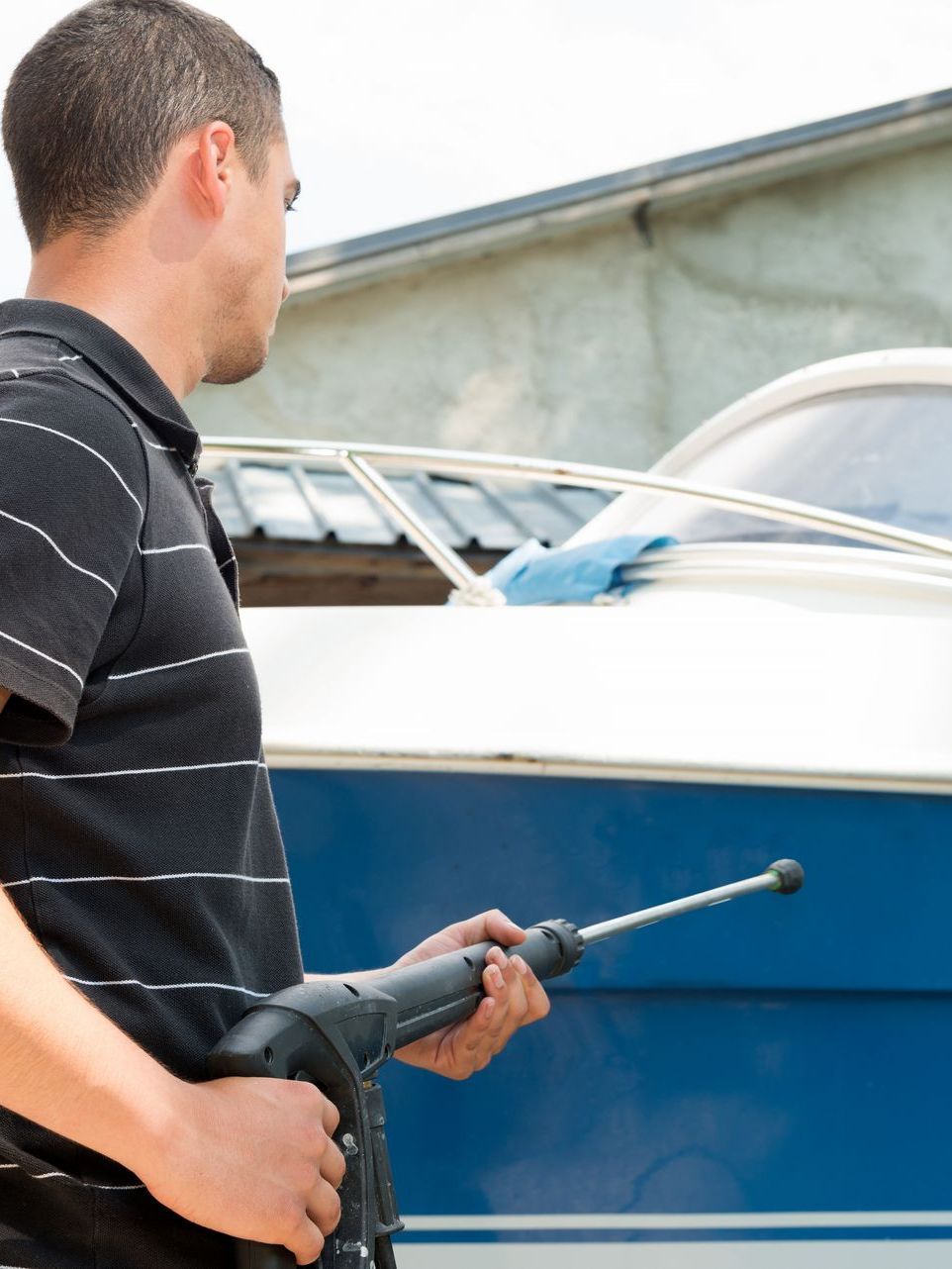 A man is holding a high pressure washer in front of a boat