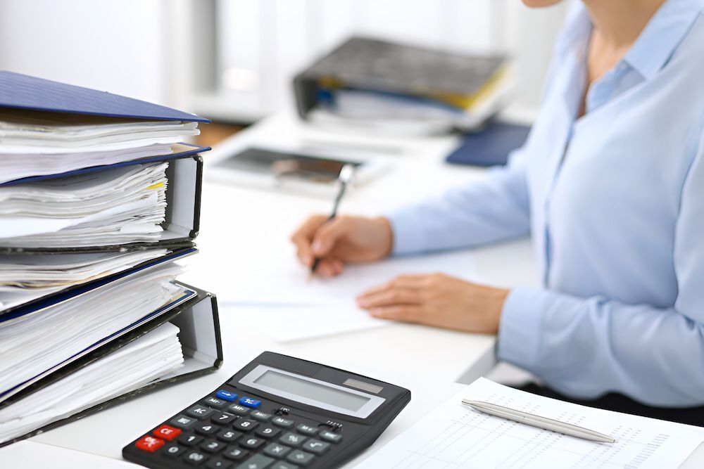 A Woman Is Sitting At A Desk With A Calculator And A Pen — BookSenz In Singleton, NSW