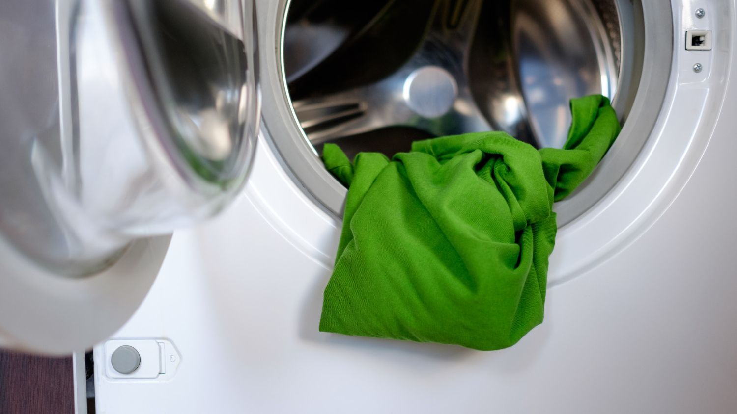 A green shirt is coming out of a washing machine.