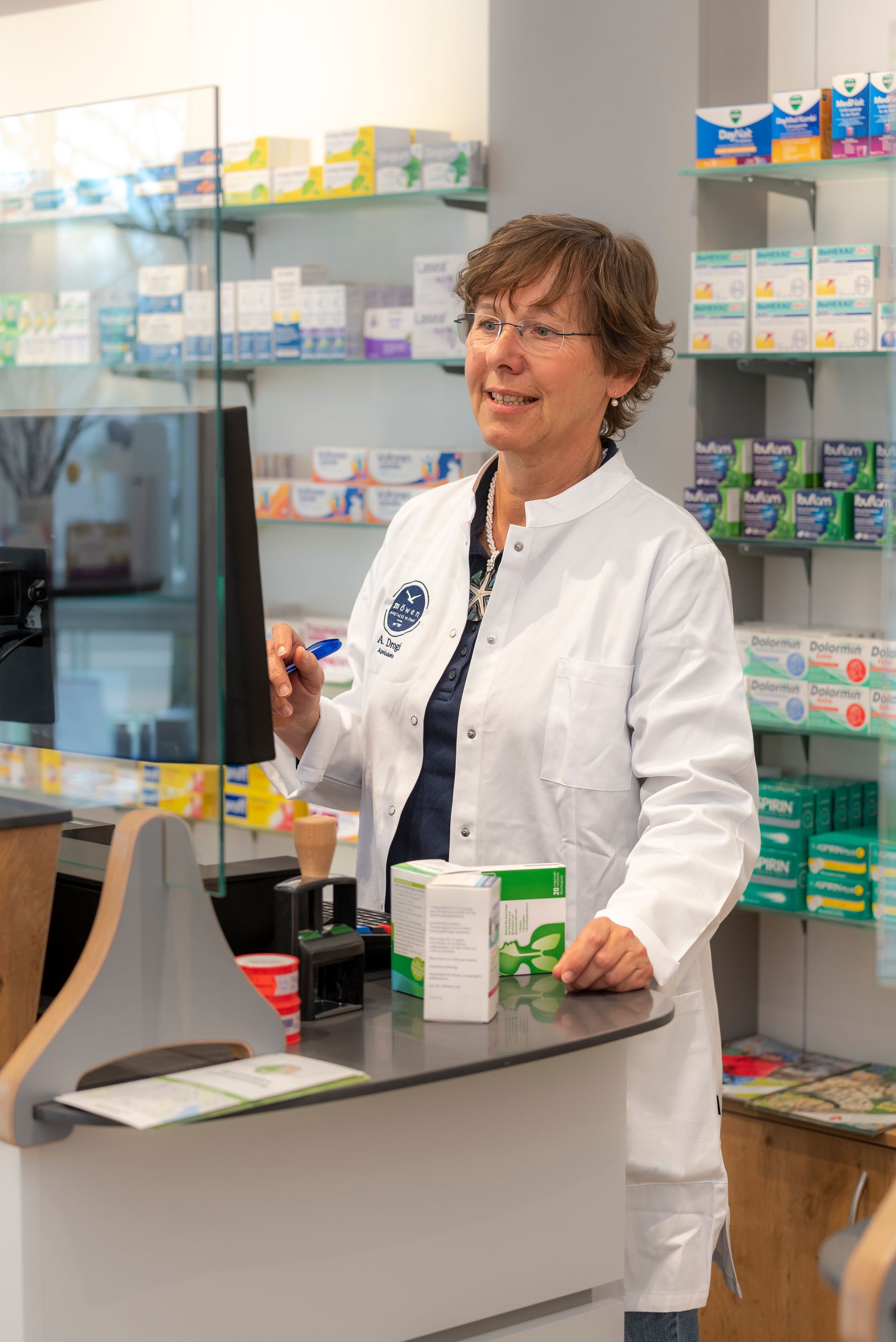 Eine Frau im weißen Kittel steht an einem Tresen in einer Apotheke.