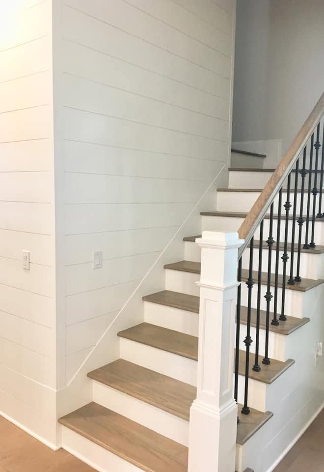 Interior staircase with white risers, wood treads, and black iron railing beside a white wall