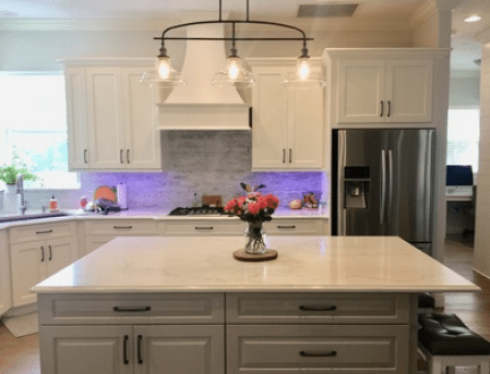 Bright kitchen with white cabinets, stainless fridge, island, and flowers on the counter