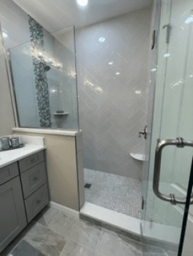 Modern bathroom with glass shower, gray vanity, and light tile flooring.