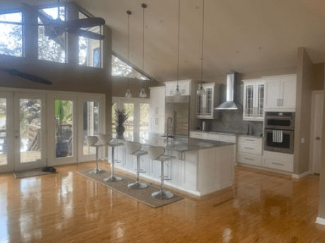 Bright modern kitchen with white cabinets, marble island, bar stools, and hardwood floors under vaulted ceilings