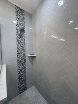 Modern shower with gray tile and mosaic accent strip, featuring a corner shelf and stone shower floor