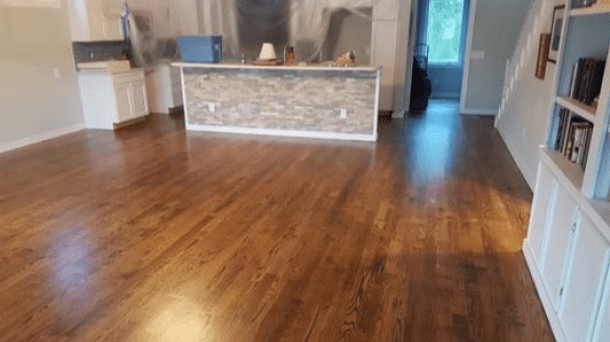 Empty wood-floored room with a stone-front counter, kitchen area, and shelves along the wall.