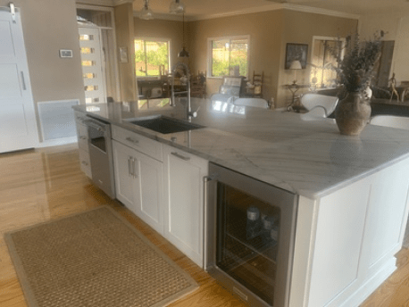 Modern open kitchen with white cabinets, marble island, wine cooler, and light wood flooring