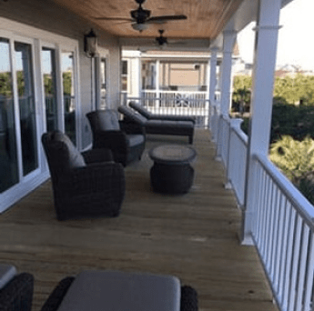 Covered porch with wicker chairs, round table, and white railing overlooking trees