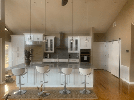 Modern kitchen with island, white bar stools, stainless appliances, and warm wood floors.