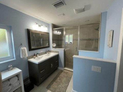 Bright bathroom with blue walls, dark vanity, large mirror, and a glass-enclosed shower.