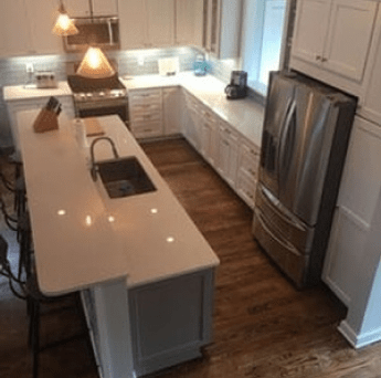 Modern white kitchen with island, hardwood floors, pendant lights, and stainless steel fridge