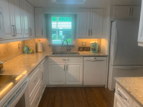 Bright white kitchen with wooden countertops, stainless fridge, and a sink under a window with blinds.
