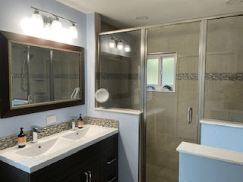 Modern bathroom with double sinks, large mirror, glass shower, and blue accent walls