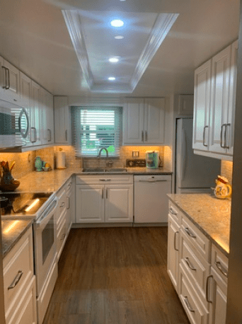 Bright white kitchen with granite counters, wood floor, and a window over the sink.