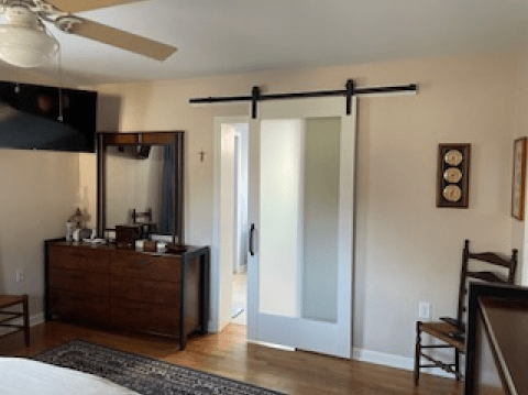 Bedroom with white sliding barn door, dresser, chair, and ceiling fan in a beige room