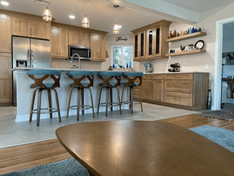 Modern kitchen with wood cabinets, island seating, pendant lights, and a dining area in the foreground