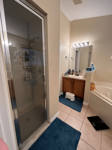 Bathroom with shower door, vanity sink, bathtub, blue rugs, and scale on tile floor