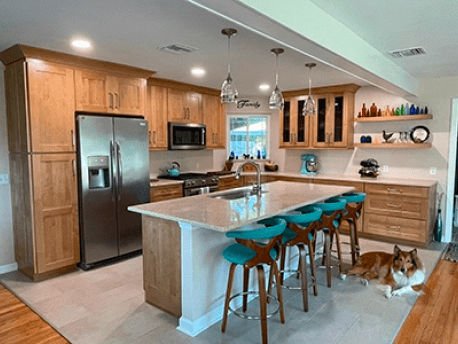 Modern kitchen with wood cabinets, island seating, stainless fridge, and a dog lying on the floor.