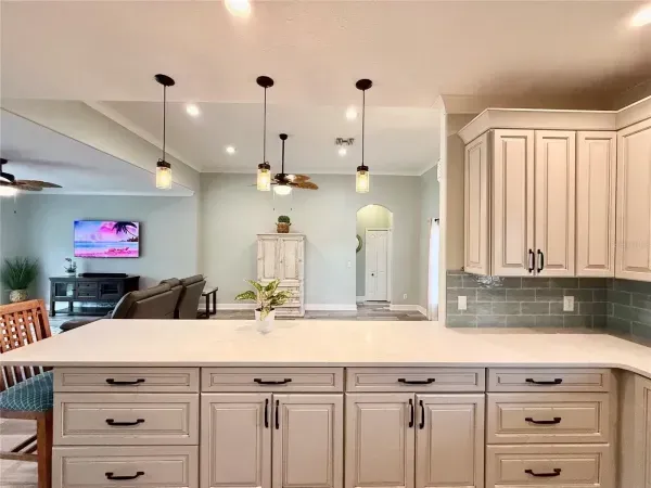 Bright modern kitchen with white island, pendant lights, and open view into a living room