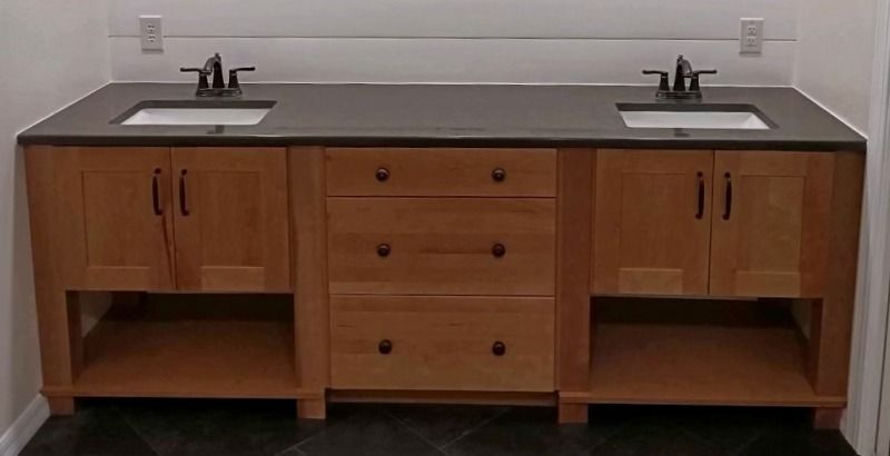 Double sink bathroom vanity with wood cabinets, dark countertop, and central drawers.