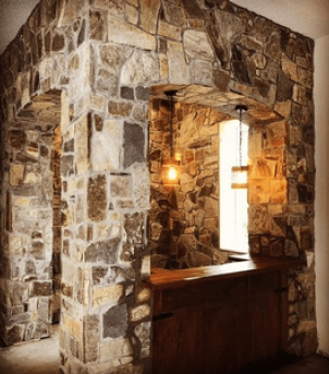 Stone-framed wooden bar nook with warm wall sconces and a bright doorway in the back