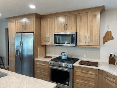 Modern kitchen with stainless steel appliances, light wood cabinets, and a black stove with a teal kettle.