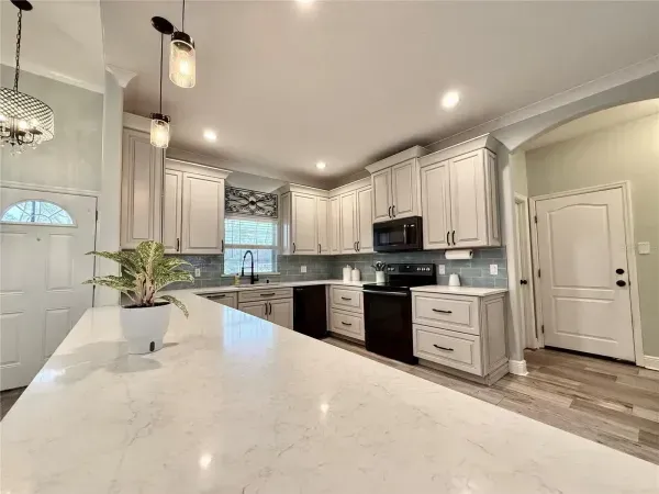 Bright modern kitchen with white cabinets, marble island, stainless appliances, and pendant lights