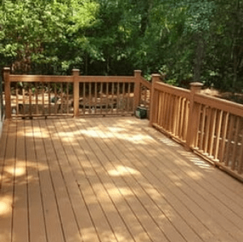 Wooden deck with railing in a wooded backyard, lit by sunlight.