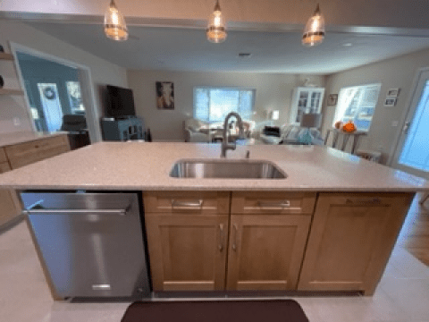 Kitchen view from an island with sink, dishwasher, wood cabinets, and pendant lights above.